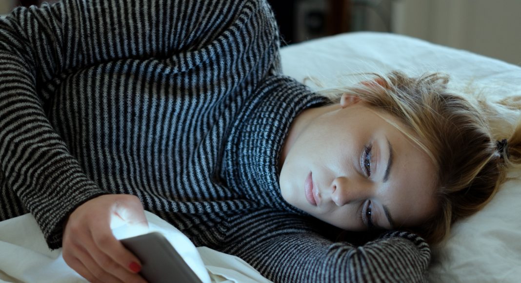 Disappointed sad girl holding mobile phone while laying on bed in a bedroom