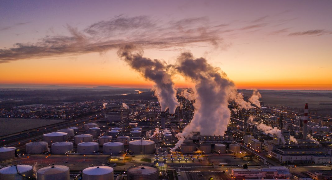 Drone point of view shot of an oil refinery under a moody sky at sunset.