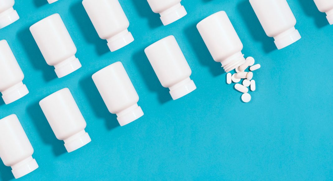 Row of pill bottles on a blue background with pills spilling out of one bottle