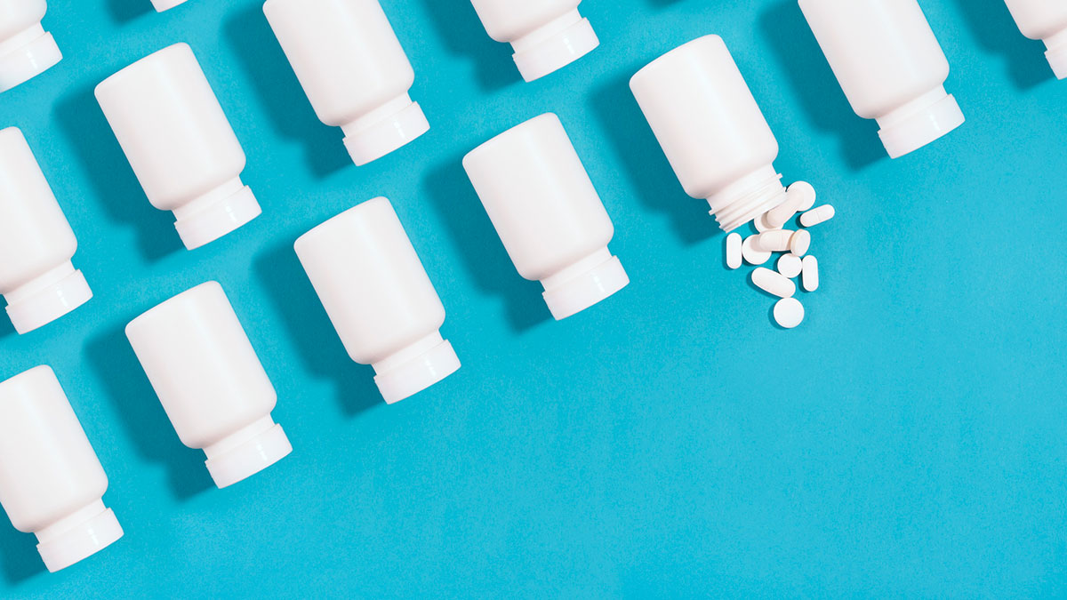 Row of pill bottles on a blue background with pills spilling out of one bottle