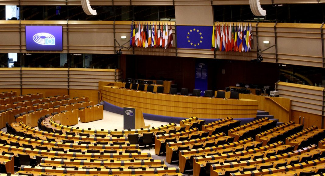 European Parliament interior in Brussels, Belgium. Empty seats in semi circle, Big screen in middle with European Union logo.