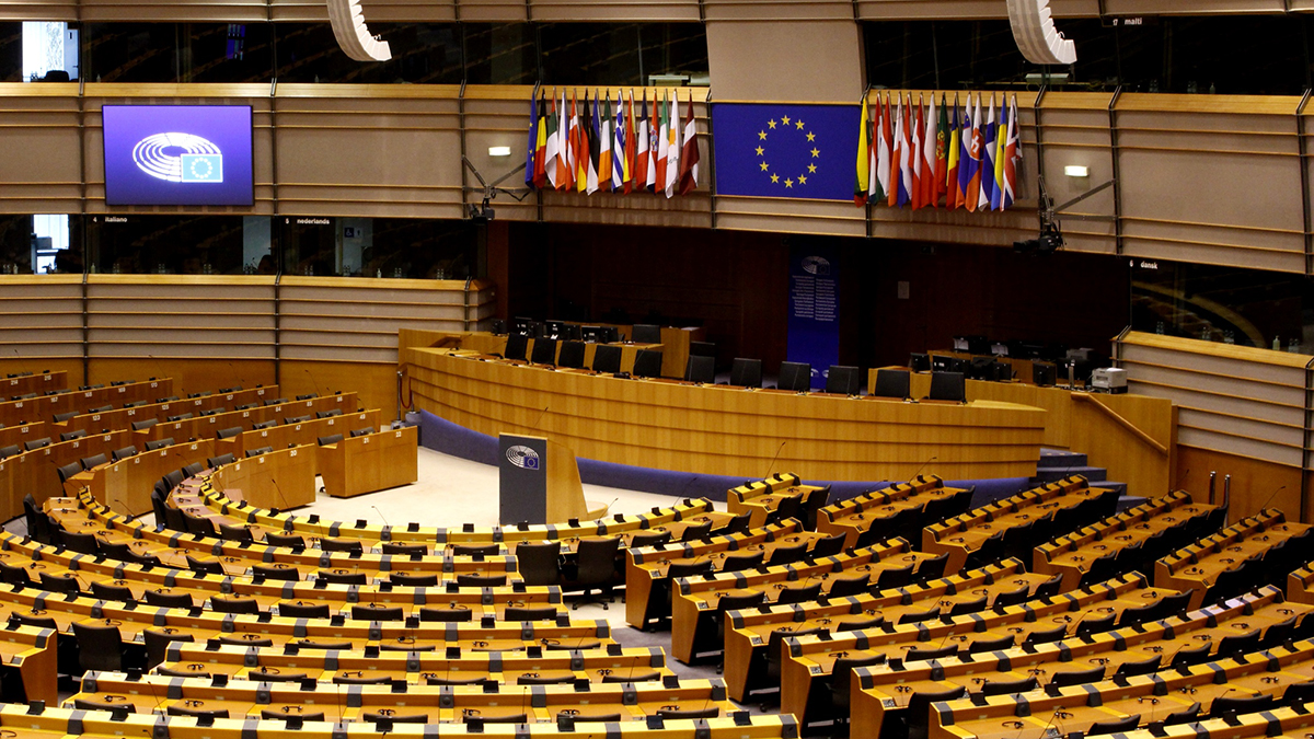 European Parliament interior in Brussels, Belgium. Empty seats in semi circle, Big screen in middle with European Union logo.