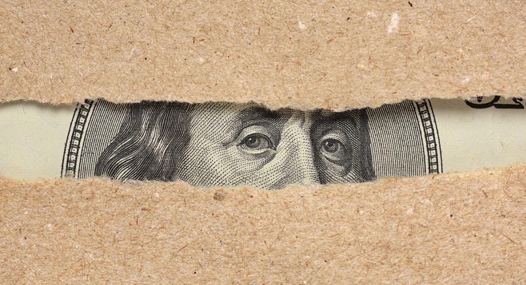 One hundred dollar bill Benjamin Franklin portrait looks behind brown craft ripped paper