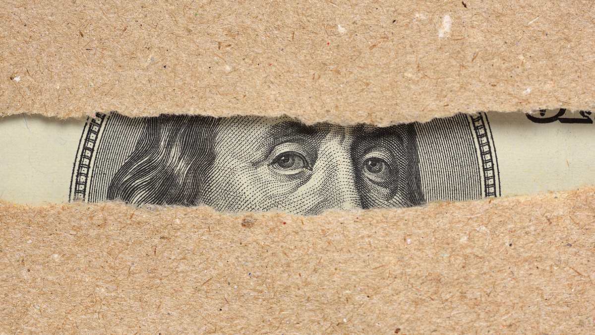 One hundred dollar bill Benjamin Franklin portrait looks behind brown craft ripped paper