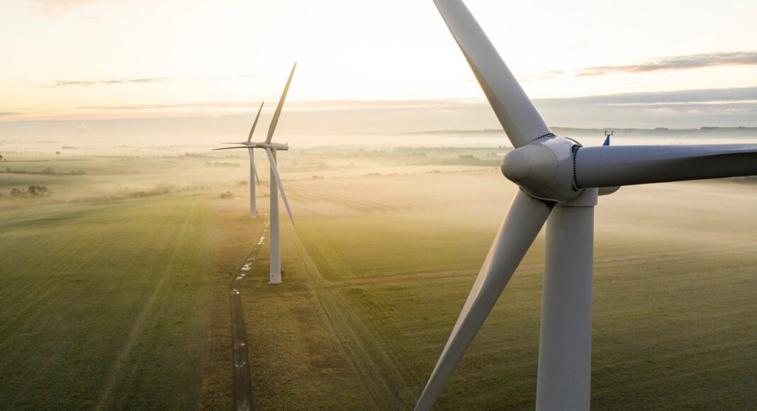 Aerial view of three wind turbines in the early morning fog at sunrise in the English countryside