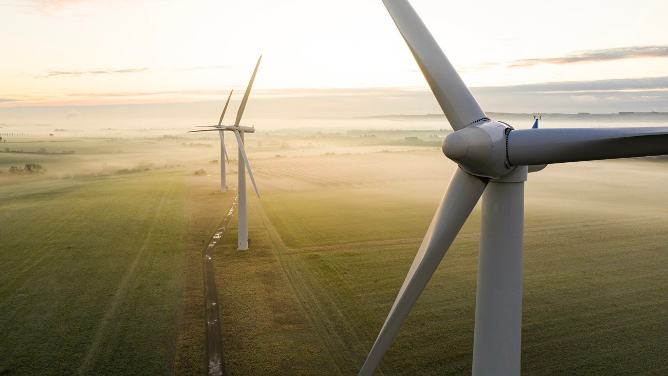 Aerial view of three wind turbines in the early morning fog at sunrise in the English countryside