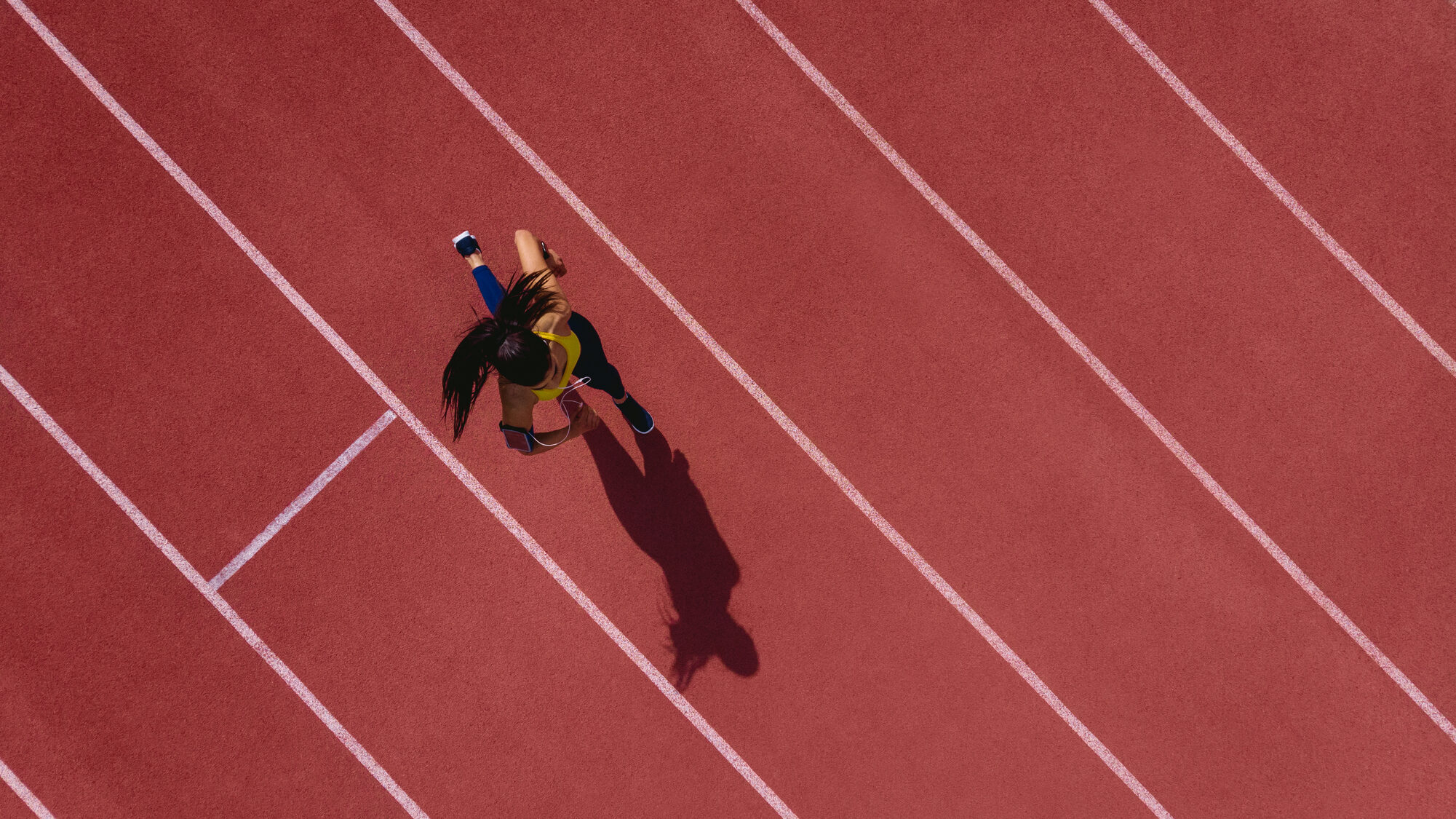 Female runner listening to music and running on sports track